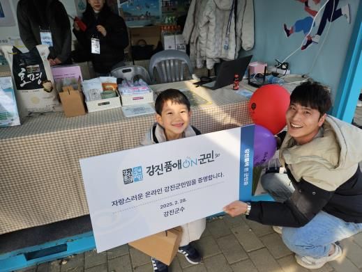 강진품애 온 군민 홍보부스에서 온라인 군민증을 들고 기념촬영을 하고 있다.